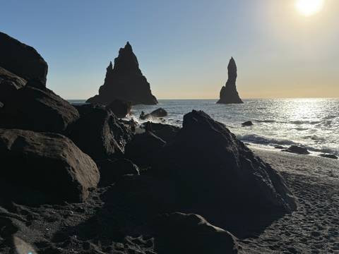 Reynisdrangar sea stacks in the ocean against a setting sun.