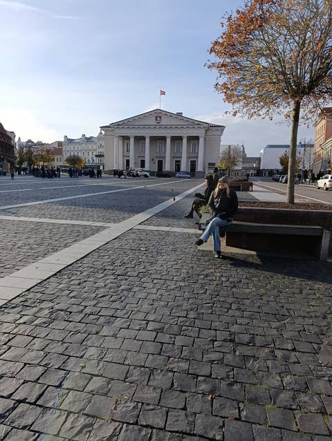 Person sitting on a bench in a large open square with historical buildings.