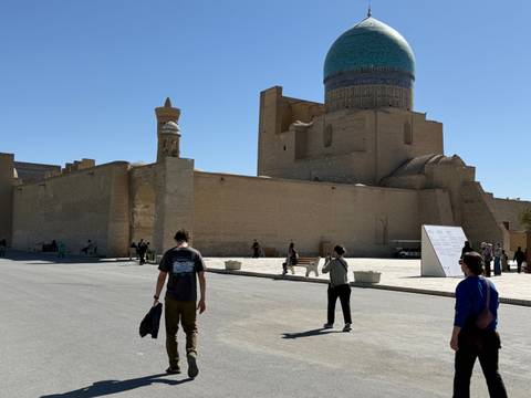       Visitors walking near an ancient city wall with blue domes.
  