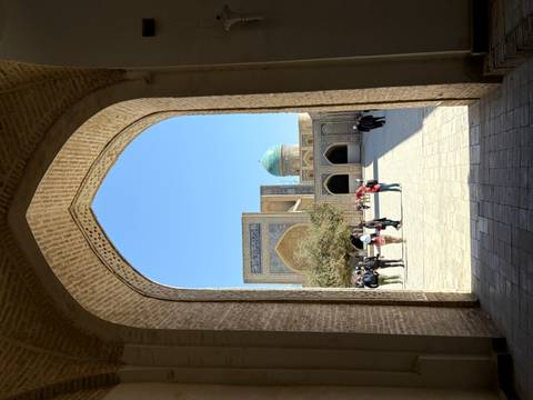 Arched doorway view of a historic courtyard with a blue dome.