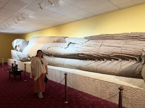 A person posing near an ancient reclining statue.