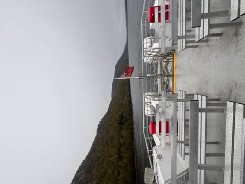       Empty ferry deck with a Union Jack flag, surrounded by calm lake water.
  
