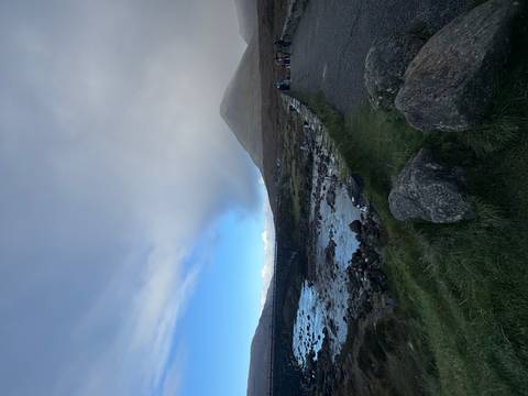       River and hills under a cloudy sky, with people exploring.
  