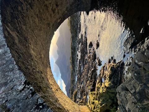       River flowing under a stone bridge with mountains in the background.
  