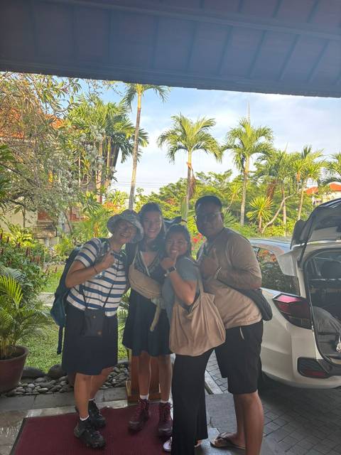 Group of four people posing with tropical plants and a parked car in the background.