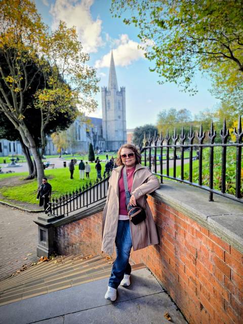      A woman posing by a fence with a historic building in the background.
  