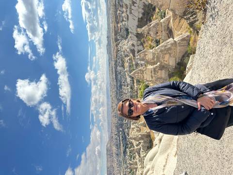 A person posing in front of a scenic landscape with unusual rock formations.