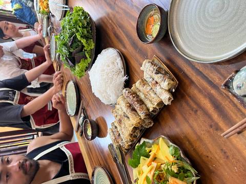 Table with spring rolls, greens, and noodles.