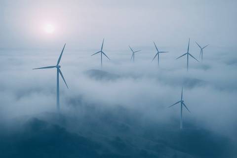 Wind turbines above a sea of clouds, with the sun visible in the background.