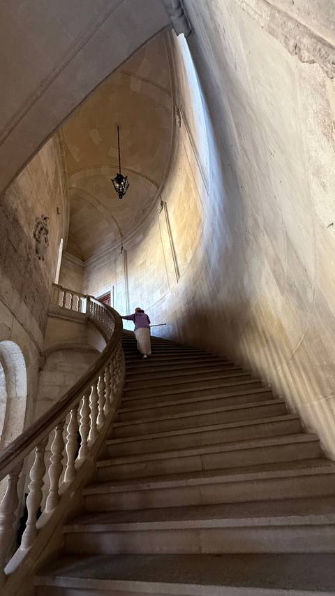 Person walking up a grand, sweeping staircase in a historic stone building.