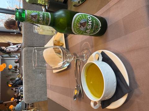       A table with a bowl of soup, Lasko beer, and people dining in the background.
  