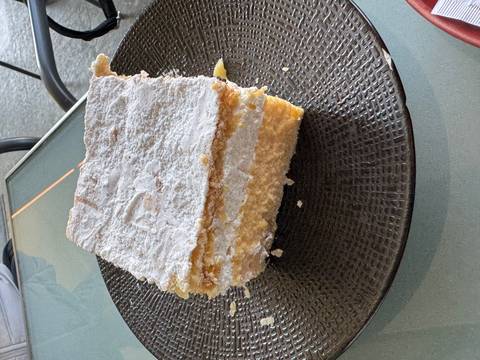       Large square piece of cream cake on a black plate.
  