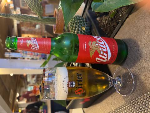       Bottle and glass of beer on a table with indoor background.
  