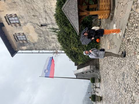       Two people with an umbrella near a Slovenian flag and a historic building.
  
