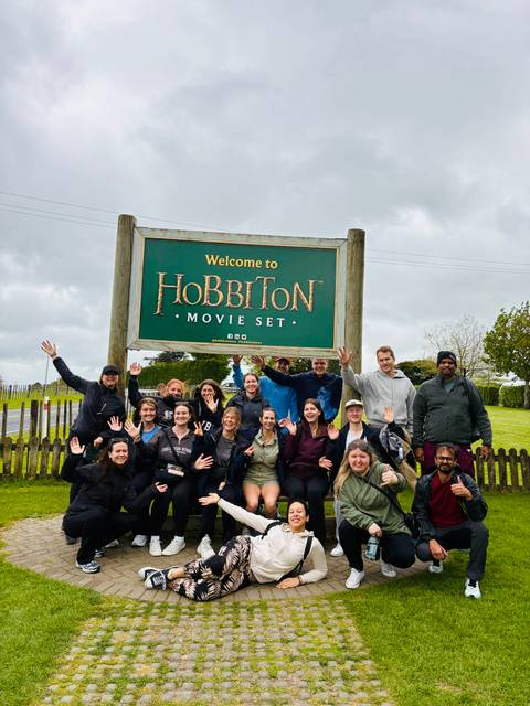       Group of people in front of Hobbiton Movie Set sign.
  