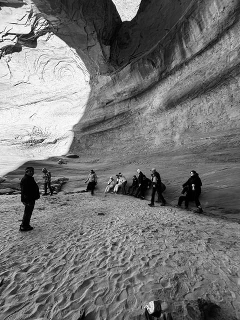 Group of people at the base of a large rock wall in a canyon.
