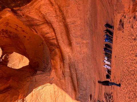       People lying on the ground in a rock cave looking up through an opening at the sky.
  