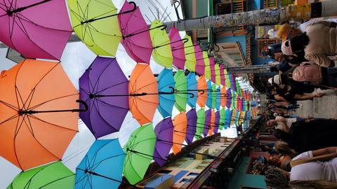       Street with colorful umbrellas hanging above, busy with people.
  