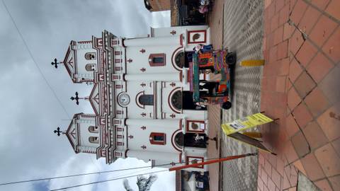 White church with red accents and a tuk-tuk passing by.