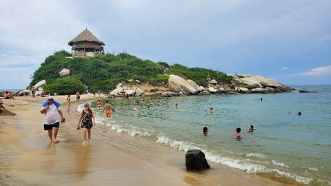       Beach scene with people swimming and a hut on a hill.
  