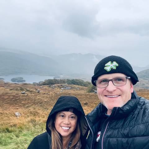 Two people in a rainy landscape with cloudy mountains in the background.