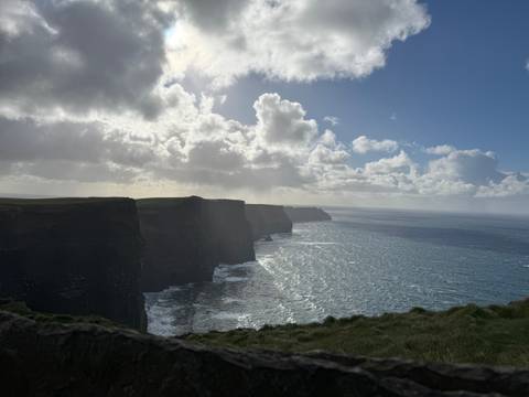 Dramatic view of cliffs meeting the ocean with a cloudy sky overhead.