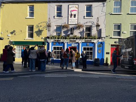 People gathering outside a brightly colored pub in a lively street scene.