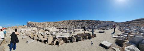       Ancient stone ruins under a clear blue sky with visitors exploring the site.
  