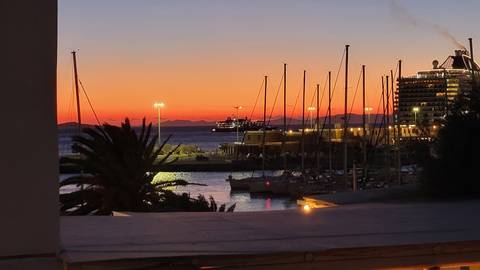       Sunset over a harbor with boats and a ship in the distance, vivid orange sky.
  