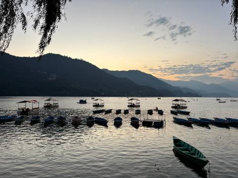 Rowboats on a calm lake surrounded by mountains at dusk.