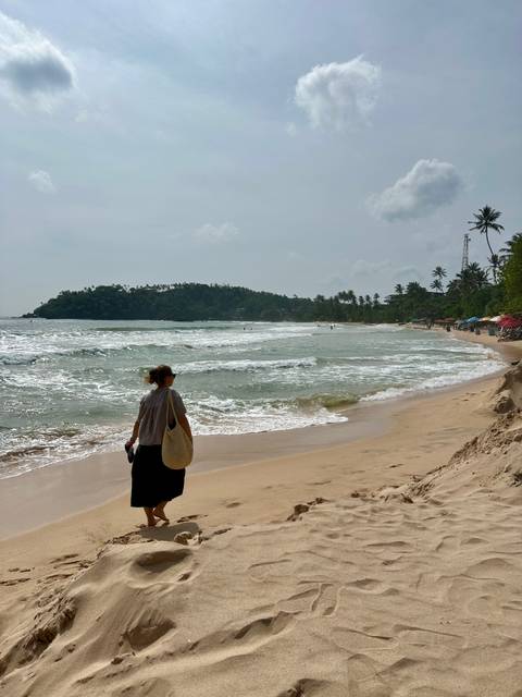 Woman walking along a sandy beach with waves.