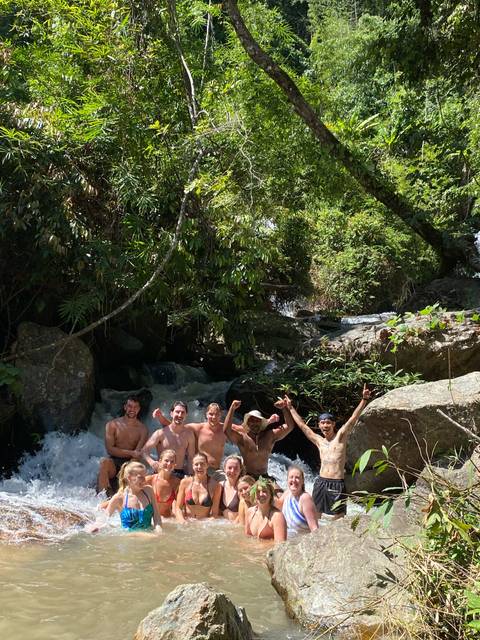       Group of people enjoying a waterfall in a tropical setting.
  