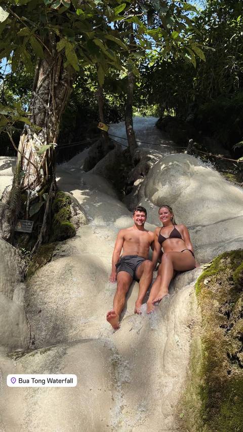       A couple sitting on smooth rocks in a natural setting.
  