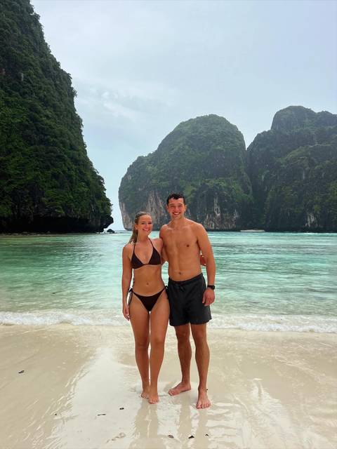       A smiling couple standing in front of a picturesque beach.
  