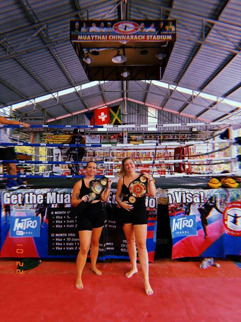       Two women posing with championship belts in a gym setting.
  