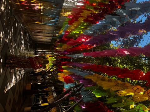       Colorful hanging decorations in a shaded outdoor area.
  
