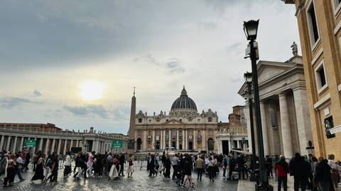 Square in Rome with a large basilica and people walking around.