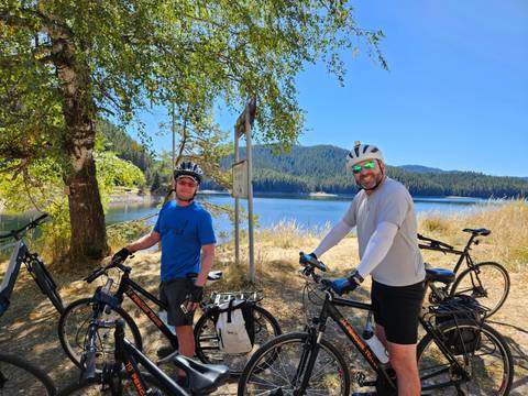 Cyclists posing by a lake with scenic hills in the background.