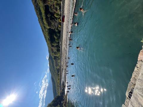 People swimming in a clear river surrounded by hills.