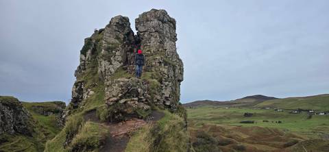 Person standing on a rock formation on a grassy hill.
