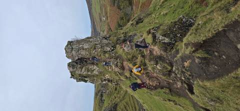 Tourists exploring a rocky hill with grassy surroundings.