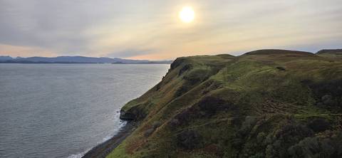 View of the ocean and hills under a setting sun.