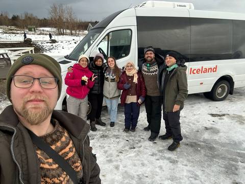Group of people in winter attire taking a selfie next to a tour bus.