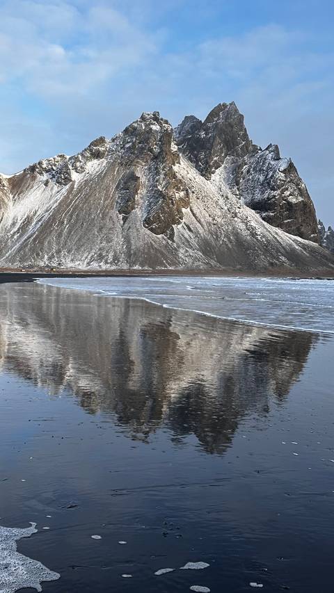       Snow-covered mountains reflecting on the calm ocean water.
  