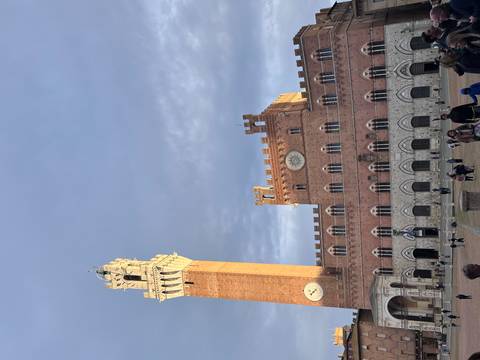 Tall brick clock tower in a square with people walking around.