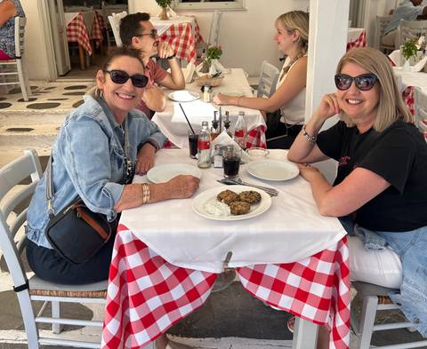       Two people sitting at a table with a checkered tablecloth eating at an outdoor café.
  