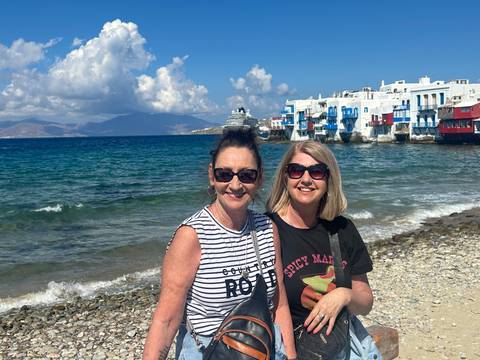       Two women posing by the sea with iconic buildings in the background.
  