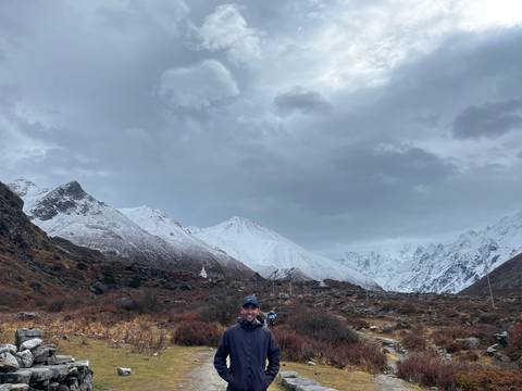       Trekker with snow-covered mountains under an overcast sky.
  