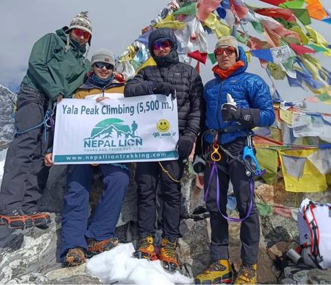       Climbers hold a sign at Yala Peak, surrounded by flags.
  