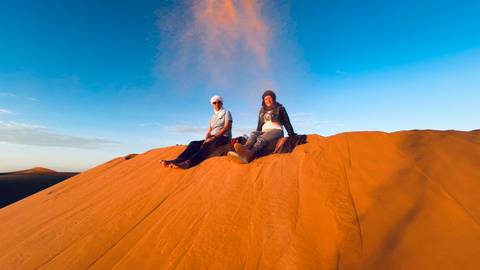       Two people sitting on a sand dune.
  
